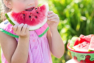 girl in pink dress eating a slice of watermelon