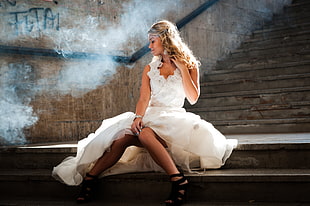woman in white sleeveless ruffle-necked dress sitting on concrete stairs beside smoke at daytime HD wallpaper