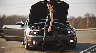 woman in black skinny pants standing in front of gray Ford Mustang sports coupe