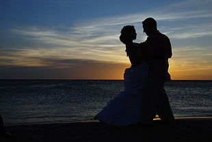 silhouette of man and woman dancing on seashore during golden hour HD wallpaper