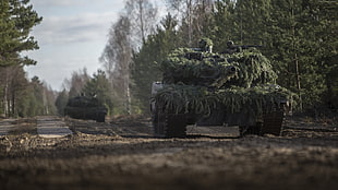 two battle tanks with green leaves camouflage on road
