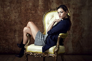 woman wearing blue cardigan sitting on white leather armchair with brown wooden frame