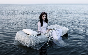 woman in black dress sits on white inflatable bed on sea