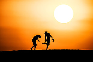 silhouette photo of two person under orange sky during sunset