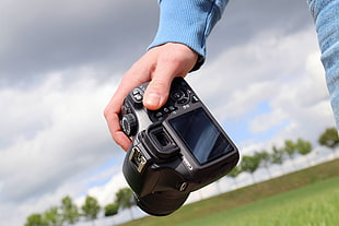 human hand holding black Canon DSLR camera