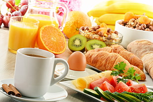 croissant and variety of sliced fruits beside pitcher and ceramic mug on white table