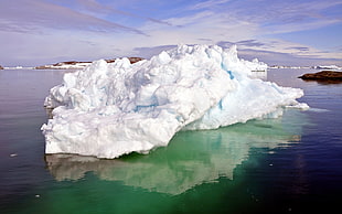 white iceberg on body of water under blue and white cloudy sky during daytime