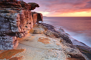 a view of cliff and body of water during sunset