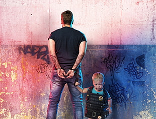 man wearing black shirt standing in front wall handcuffed by toddler in black vest