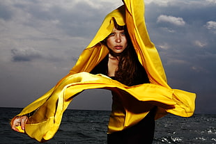 woman in black dress with white scarf standing in near body of water