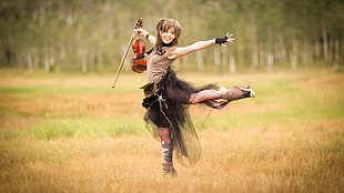 woman wearing black lace crew-neck top and tutu skirt holding violin and bow with hands stretching out