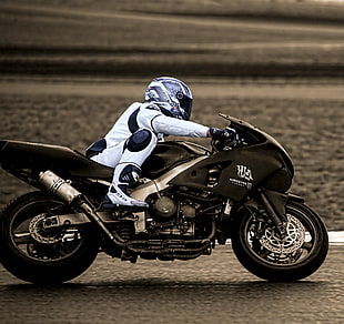 timelapse photography of man riding black sports bike wearing white motorcycle gear on black asphalt pavement