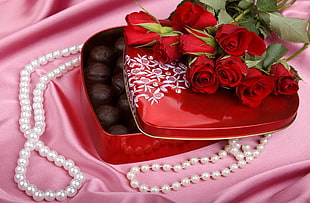 bouquet of red roses on top of black steel chocolate case filled with round chocolates