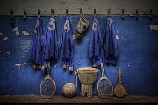 photo of five blue jacket hanging on wall hooks and five assorted sports gear on floor