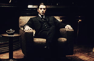 man's in black suit sitting on armchair
