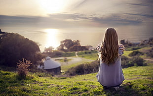 selective focus photography of a girl watching body of water on hill