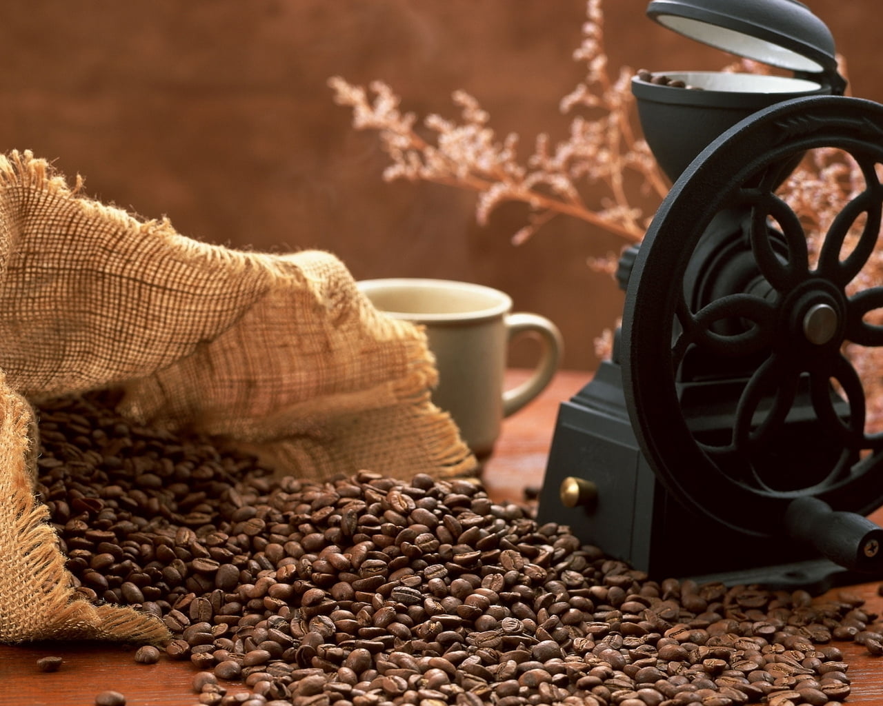 spilled coffee beans in sack beside black machine and white ceramic mug