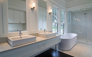 photo of white wooden sink with mirrors beside freestanding bathtub