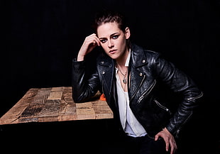 woman wearing black leather jacket leaning on brown table