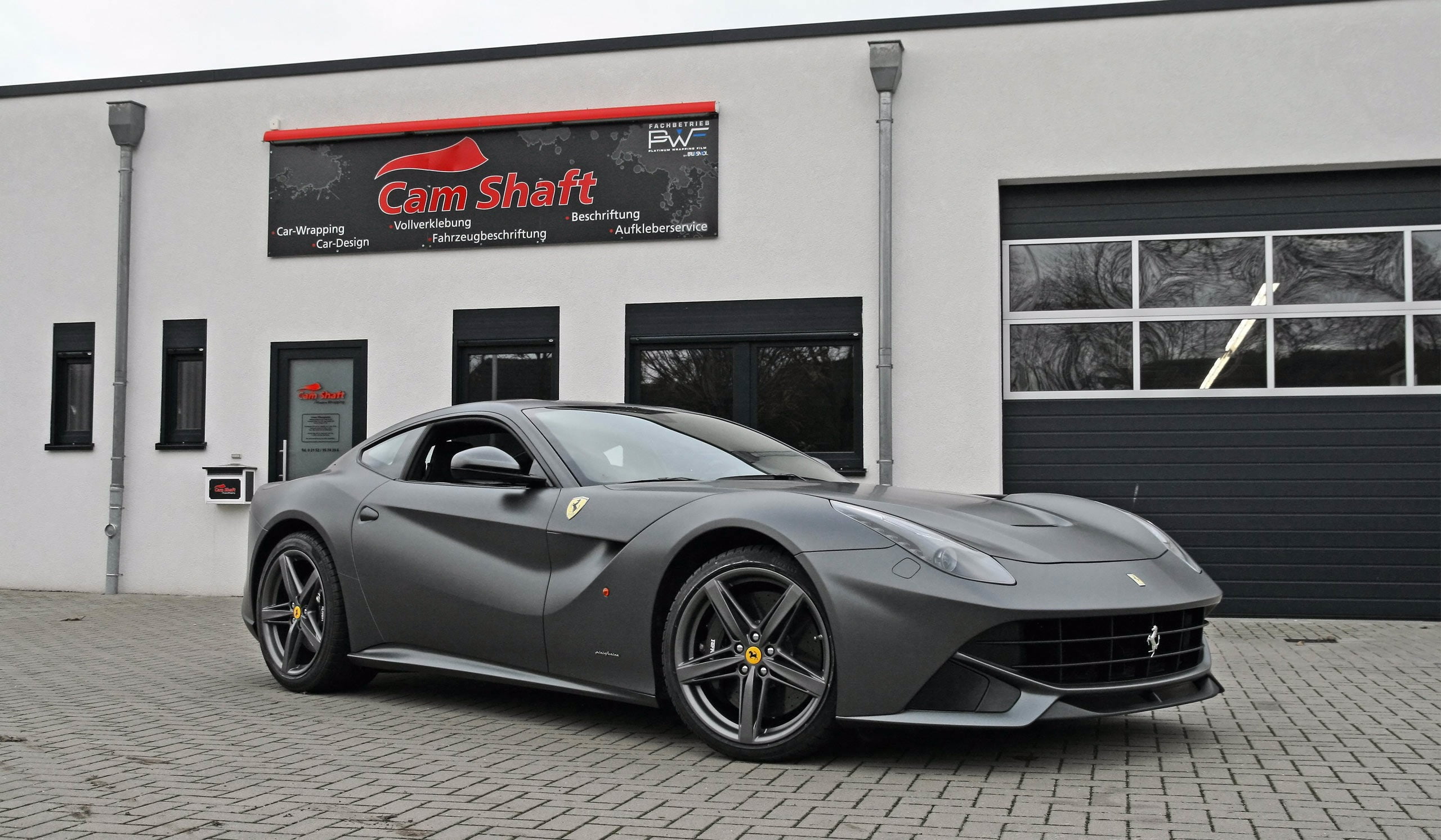 gray Ferrari sports coupe parked beside white concrete building