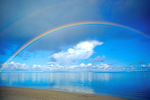 blue body of water with rainbow under blue skies
