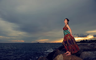 woman wearing red and green floral sleeveless maxi dress standing on seashore