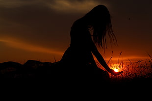 silhouette view of woman sitting on grass fields