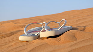 two white flip-flops on desert during daytime