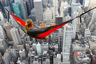 woman laying in red and black hammock above high-rise buildings HD wallpaper