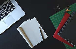 black ballpoint pen on top of white notebook near MacBook Pro