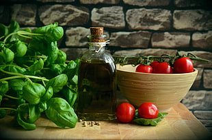 still life photography of red tomatoes on brown ceramic bowl beside glass bottle filled with black liquid HD wallpaper