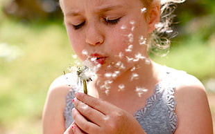 close-up photography of girl blows a white dandelion flower at daytime