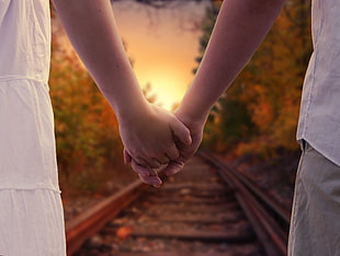 two person holding hands walking on trail rail during golden hour HD wallpaper