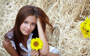 brown haired woman in white sleeveless blouse holding a sunflower