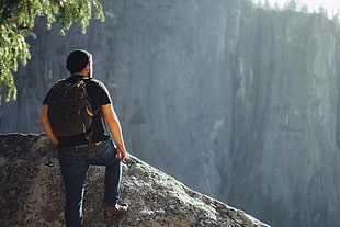 man on top of rock formation wearing black backpack and shirt