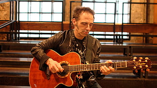 man wearing black leather jacket holding brown acoustic guitar
