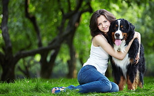 Woman wearing white tank top hugging dog on the grass during day time\