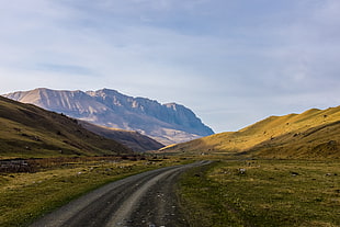 road leading through mountain under grey clouds HD wallpaper