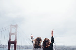 two woman throwing peace signs near golden state bridge during daytime