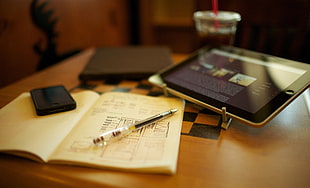 black iPad near book and pen