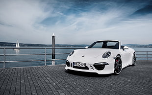 white Porsche 911 convertible parked near gray fence overlooking sea