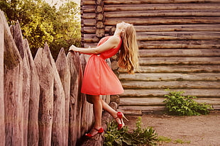 woman in red sleeveless dress on wooden fence posing for photo