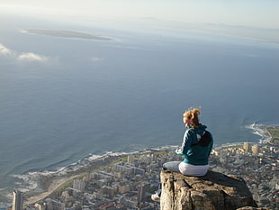 woman in blue jacket sitting on rock near ocean at daytime