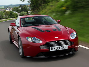 red Aston Martin sports coupe on gray concrete road near grass during daytime HD wallpaper