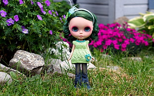 green haired and green dressed girl doll on gardenfield during daytime