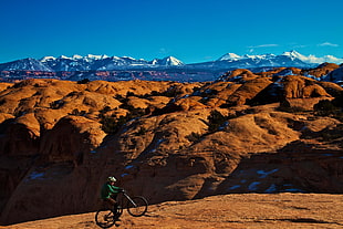person riding bicycle on brown land within mountain range during daytime