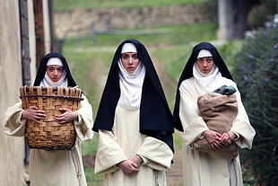 three nun walking near hedge carrying bags during daytime