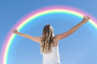 brown haired woman wearing white tank top raising her two hands over the rainbow
