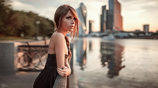 woman in black and grey dress standing near calm body of water and concrete buildings during daytime