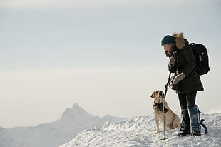man wearing black jacket standing beside brown dog